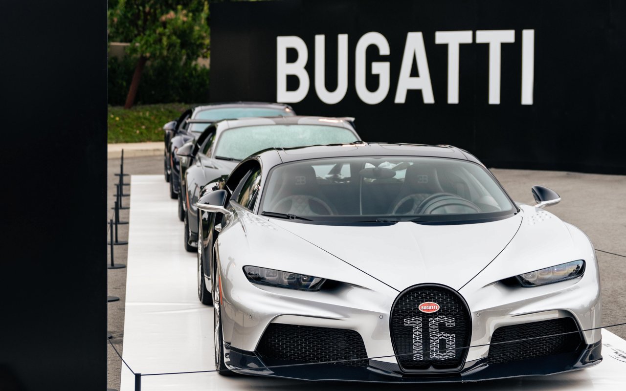 Three Bugatti cars in line at the Pebble Beach event. Black wall with white BUGATTI tag in the background.